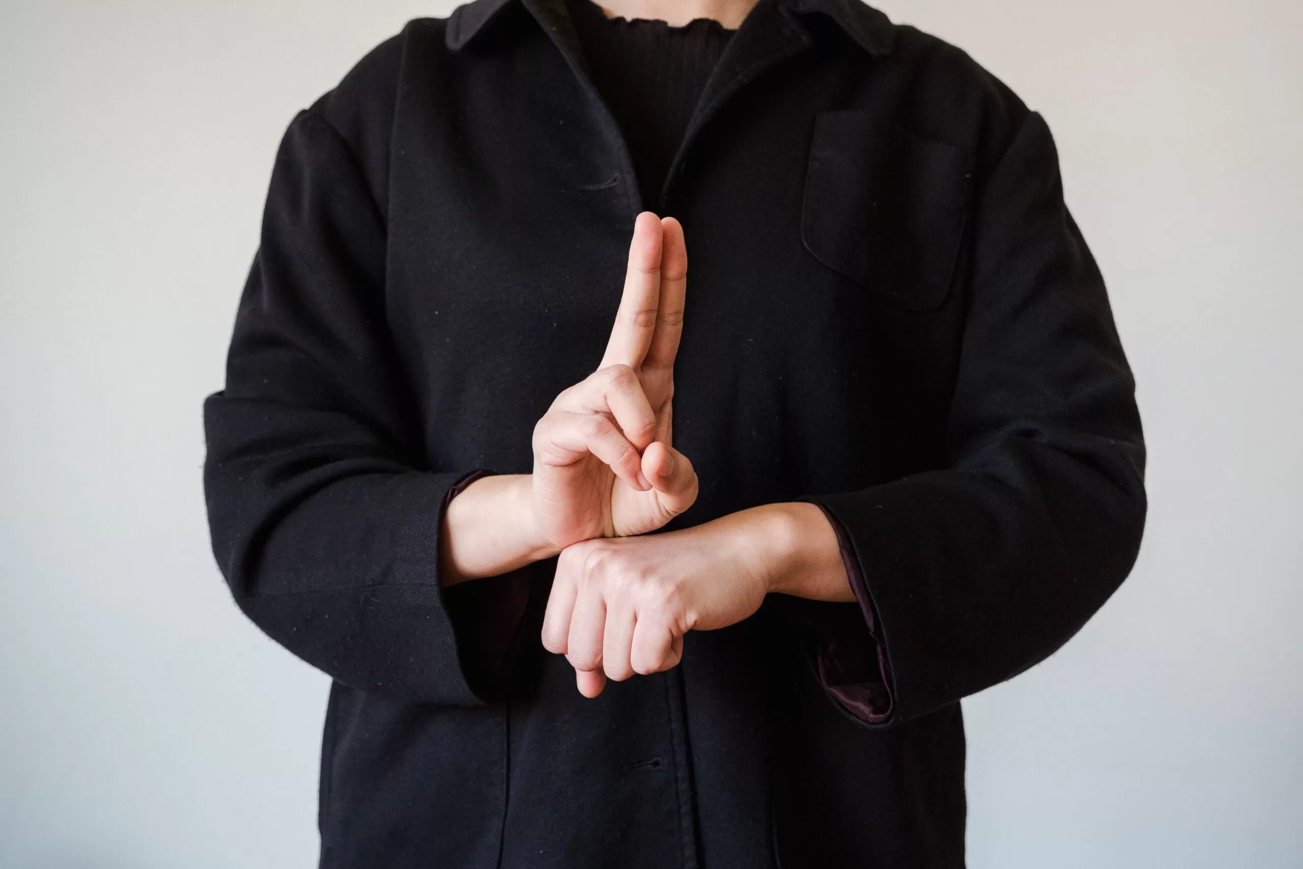 Person in a black shirt makes a hush gesture with an upright index finger.