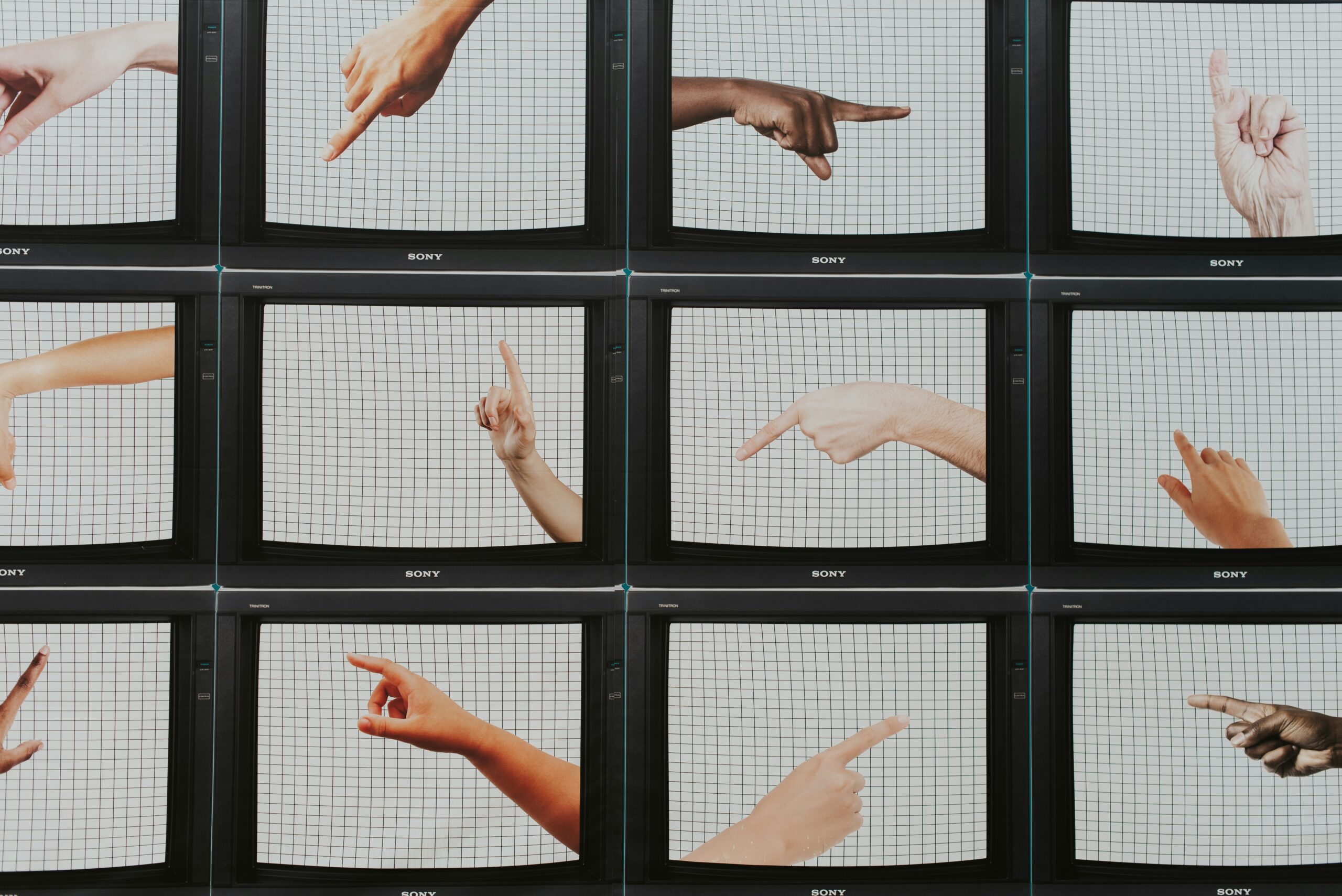 Row of vintage Sony CRT TVs with hands pointing in different directions against a grid backdrop.