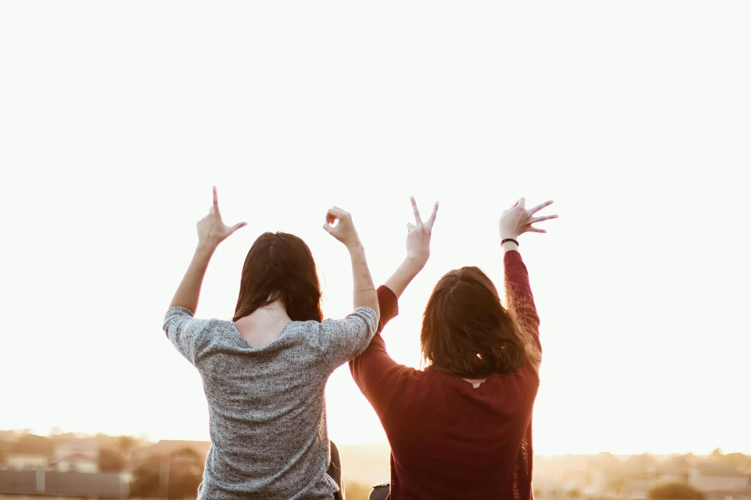 Three people shown from behind with arms raised in the air at sunset, celebrating outdoors.