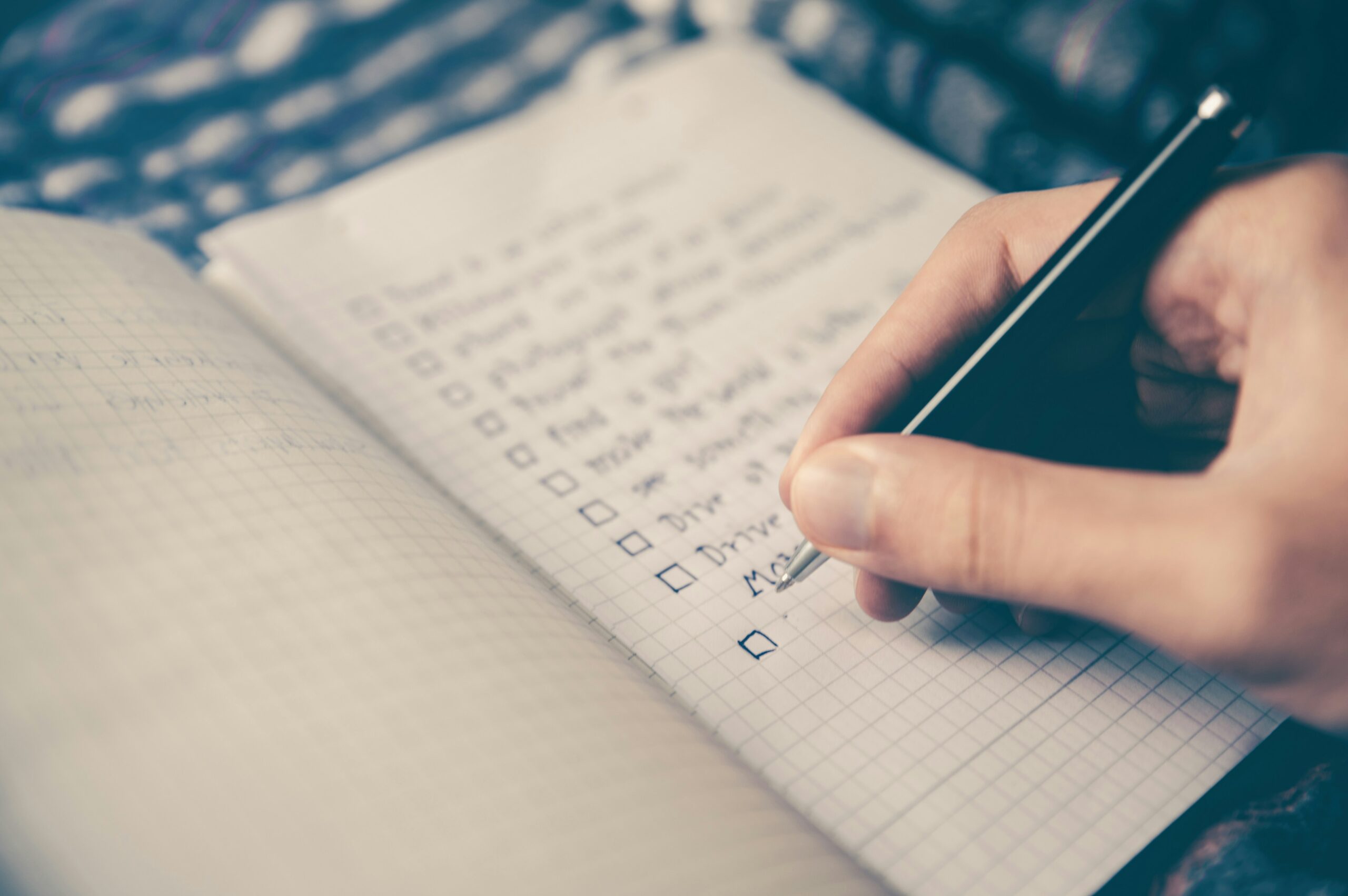 Close-up of a hand holding a smartphone over a notebook page with checked boxes on a list trayed as a to-do list.