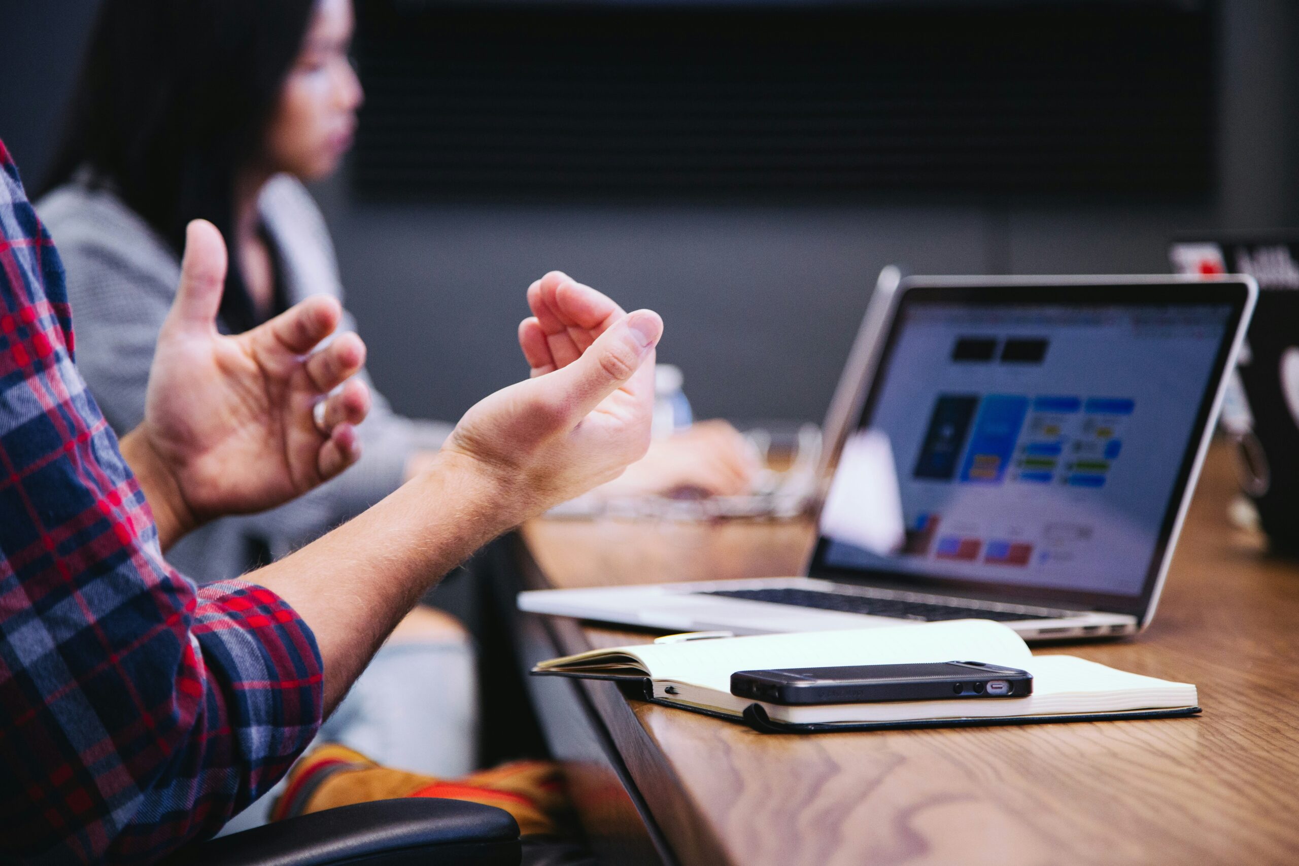 Close-up of hands gesturing during a meeting, with a laptop and notebook on the table in view