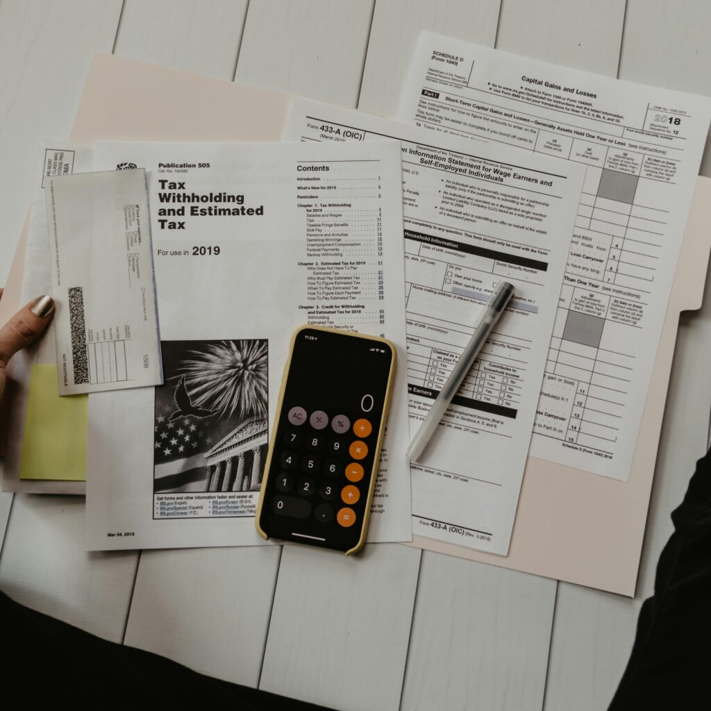 Person working at a desk with tax documents, a calculator, and a smartphone on light-colored wood flooring